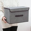 A gray fabric storage box is held by a person wearing a cream-colored knit sweater.