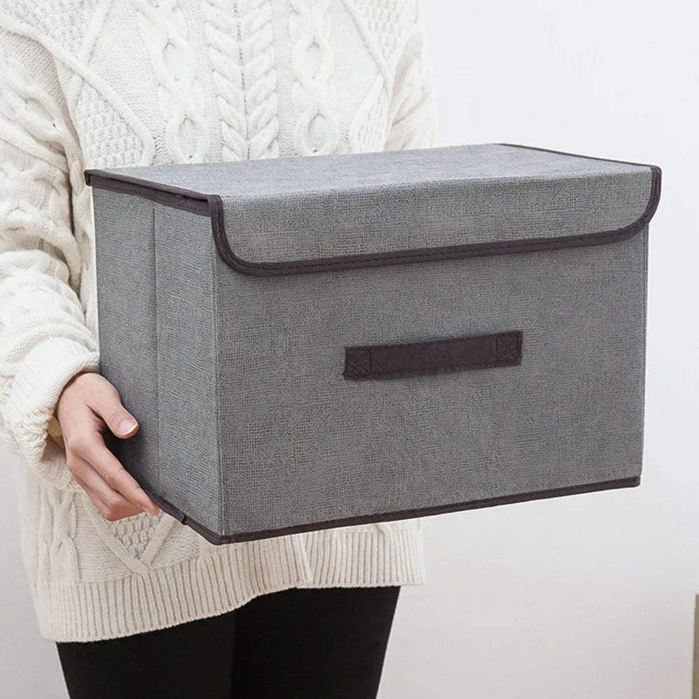 A gray fabric storage box is held by a person wearing a cream-colored knit sweater.
