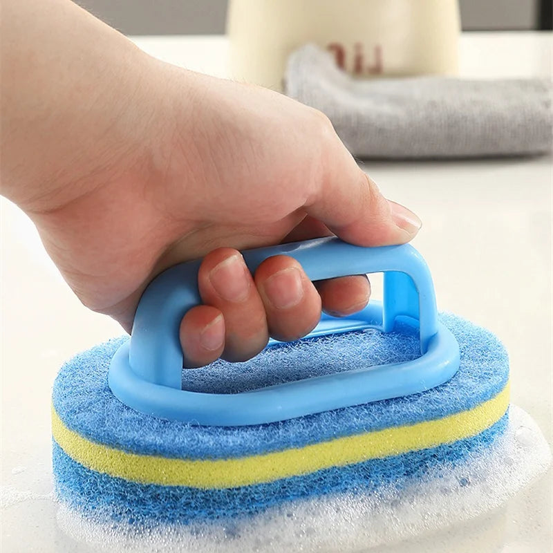 A hand holds a blue sponge cleaning brush with a yellow band on a white surface.