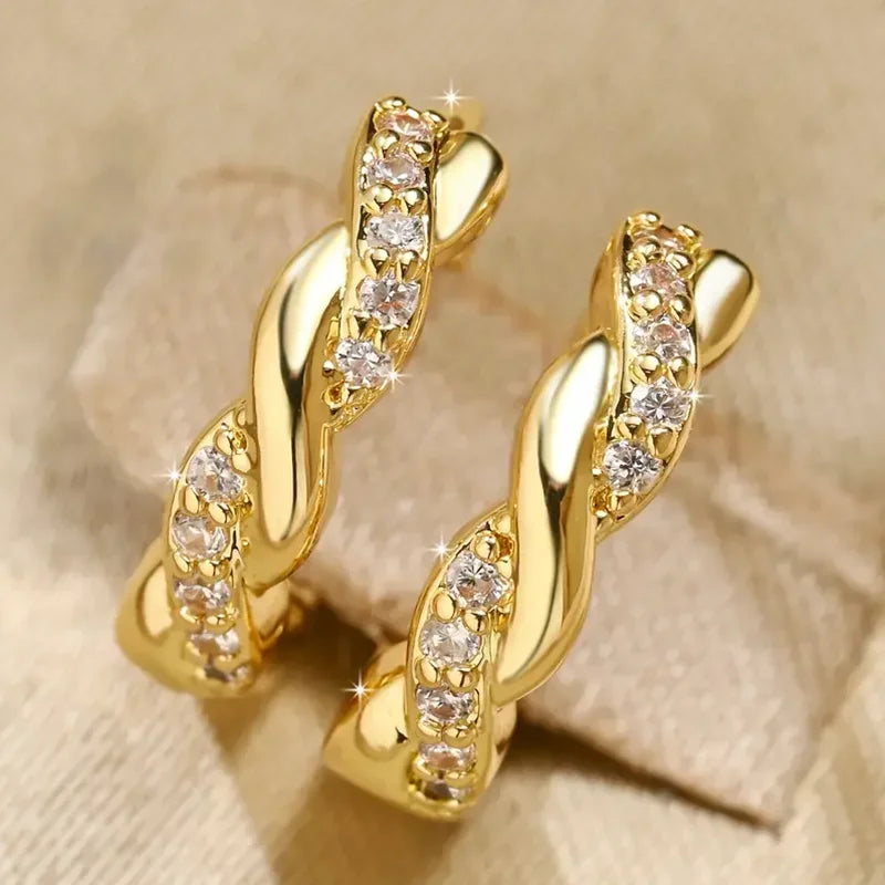 Par de aretes tipo aro dorados con diseño trenzado y piedras de circonita cúbica transparente.