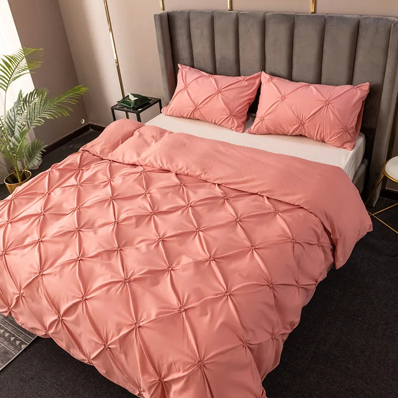 A pink 3D pinch pleated duvet cover set displayed on a bed with gray upholstered headboard and pillows.