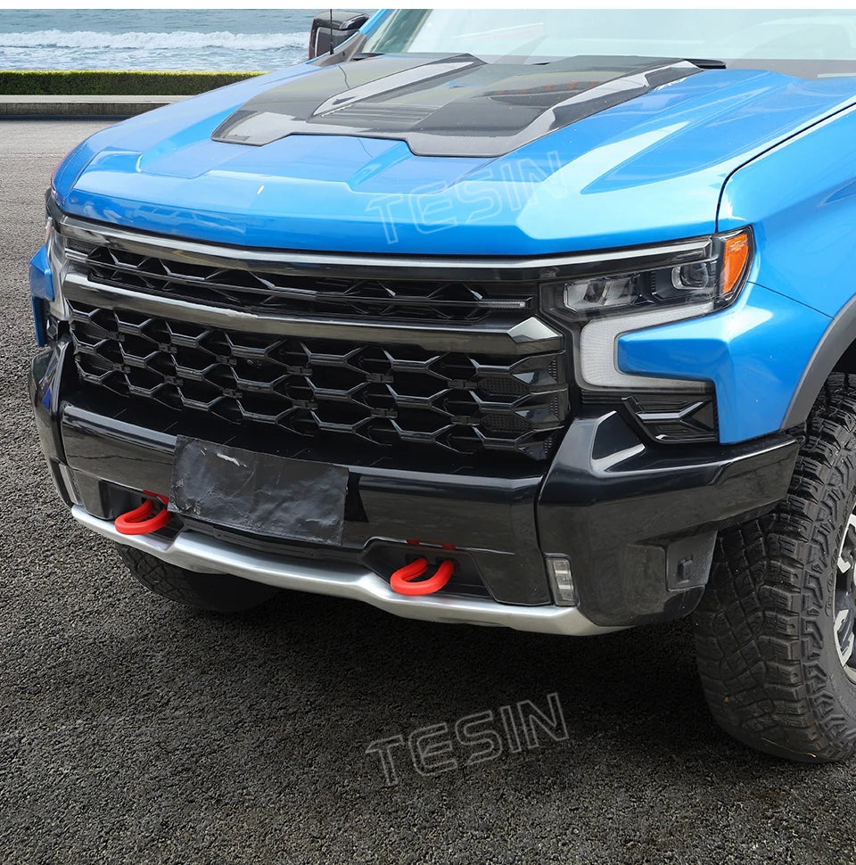 Close-up of a blue Chevrolet Silverado front bumper with an aftermarket black tow hook cover installed.