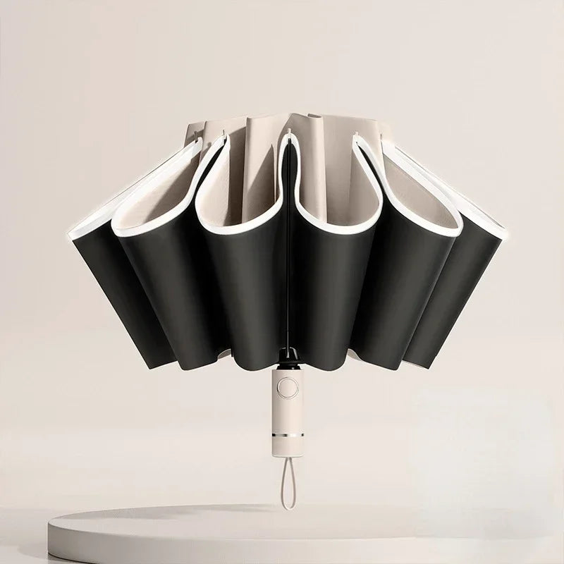 A black fully automatic reverse-folding windproof umbrella with white accents is displayed on a light surface.