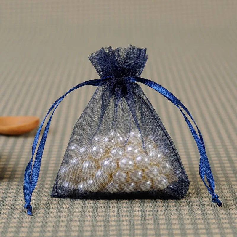A sheer blue organza drawstring gift bag filled with white pearls, tied with a matching blue ribbon.