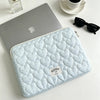 A light blue quilted laptop sleeve is placed next to a silver laptop and sunglasses on a white surface.