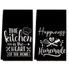A set of two black kitchen towels featuring white text slogans like The kitchen is the heart of the home and Happiness Homema