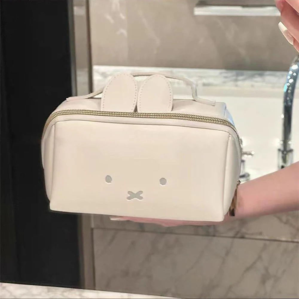 A beige Miffy cartoon rabbit cosmetic storage bag with a zipper is held in a hand in a bathroom setting.
