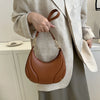 A woman holds a brown leather crossbody bag with a gold chain strap against a light beige blazer.