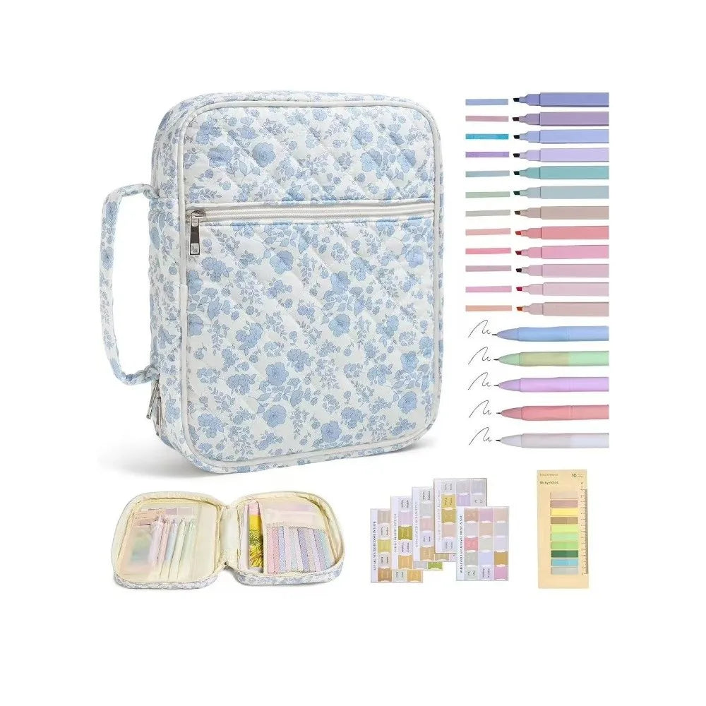 A light blue floral quilted Bible cover with a zipper pocket and carry handle, shown next to various colored pens and pencils