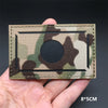 A rectangular camouflage patch with a circular black center and hook-and-loop backing is held in a hand.