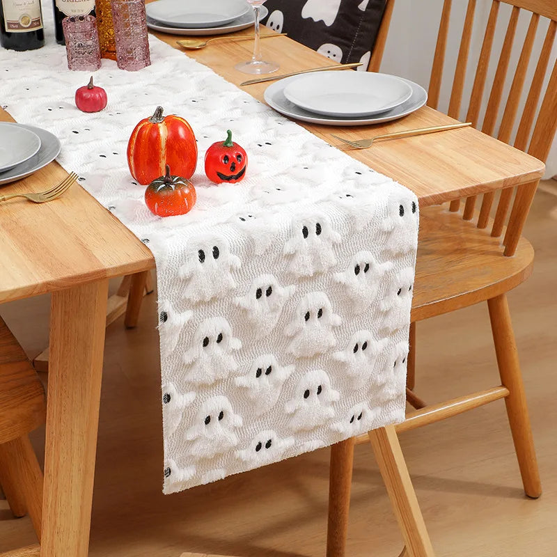 White table runner with black ghost pattern and autumn pumpkins on a wooden table.