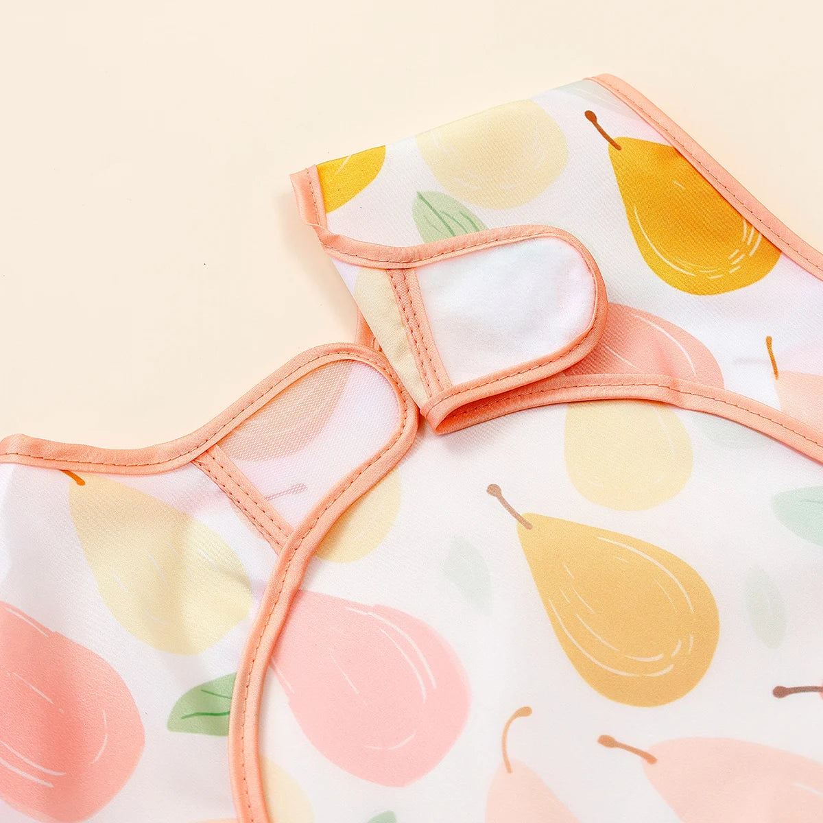 A peach and yellow patterned waterproof full-body baby feeding bib with a sleeveless design.