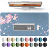 A waterproof PU leather desk pad featuring a keyboard and mouse, surrounded by scattered pink petals and various colored circ
