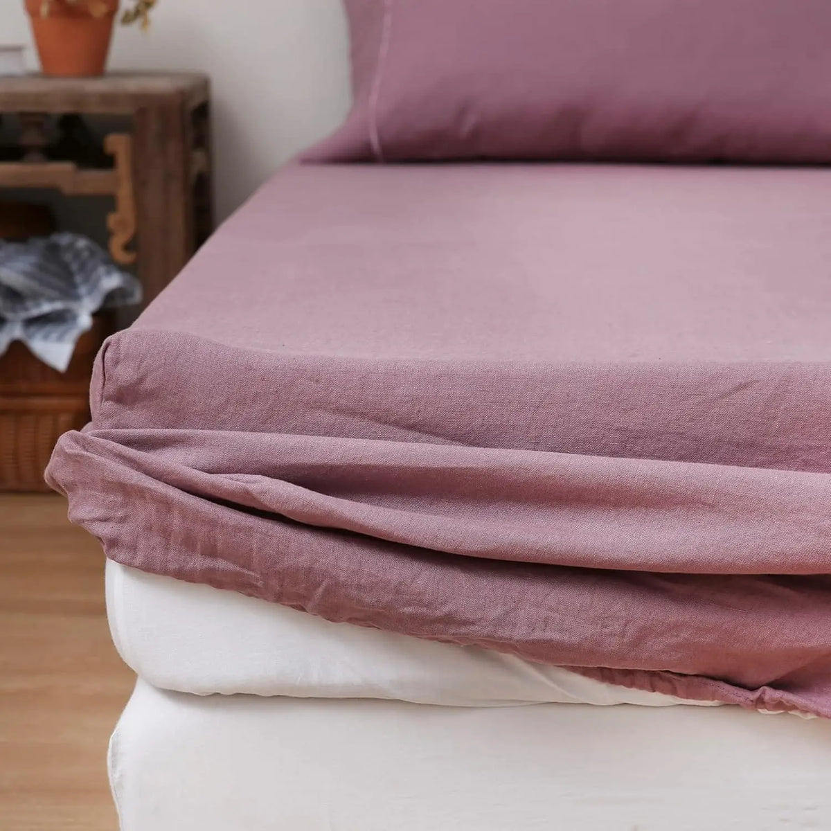 A folded mauve linen fitted sheet draped over a white mattress.