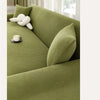 A close-up of a moss green stretch jacquard sofa cover with textured fabric and a white decorative pillow.