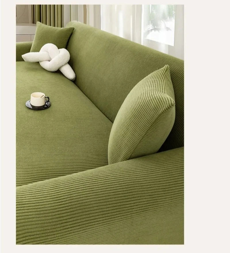 A close-up of a moss green stretch jacquard sofa cover with textured fabric and a white decorative pillow.