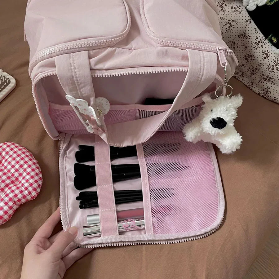 A pink cosmetic travel organizer bag with a zippered compartment and an open section displaying makeup brushes and a white be