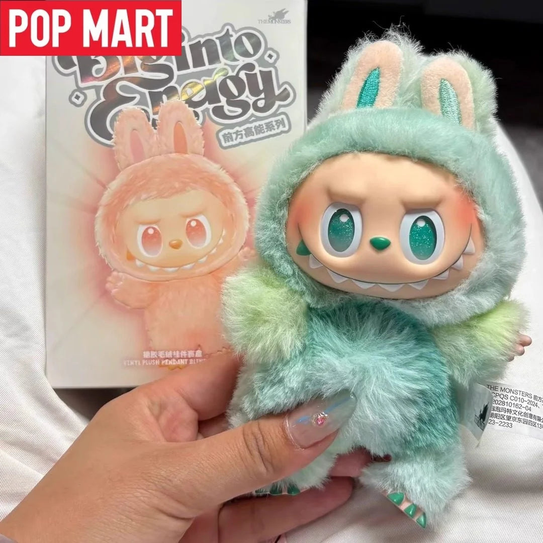 A soft green plush doll resembling a rabbit face is being held in a hand against a product box.
