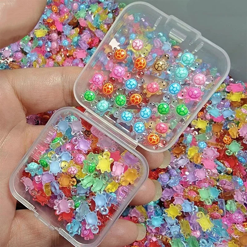 A hand holds two clear plastic containers filled with glow-in-the-dark mini turtle figurines in various bright colors.