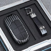 A black carbon fiber key fob cover with a metal keychain attached, displayed in a square box.