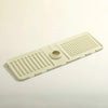 A beige silicone faucet draining mat with raised ridges and a central drain hole.
