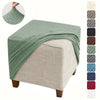 A green stretch jacquard ottoman slipcover draped over a beige upholstered ottoman.