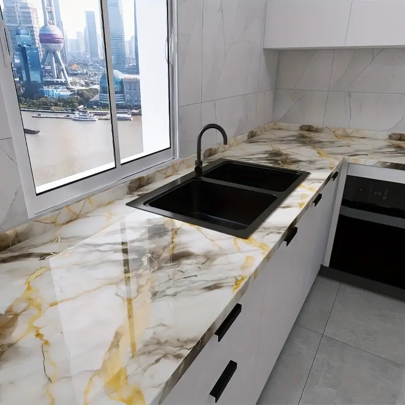 A kitchen countertop made of white marble contact paper with gold veining and a black sink.