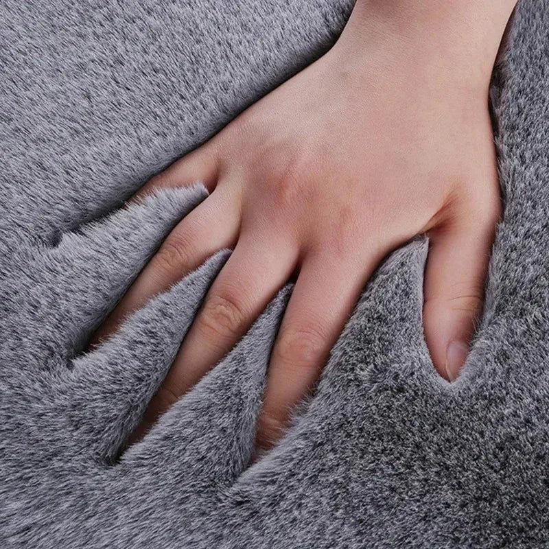 A hand is gently touching a gray plush rabbit fur car seat cushion.