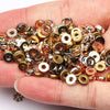 A hand holds a pile of small round acrylic spacer beads in various gold and silver tones for jewelry making
