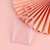 Sujetador de tarjetas de acrílico transparente con borde rosa y llavero, sobre fondo de papel plisado rosa.