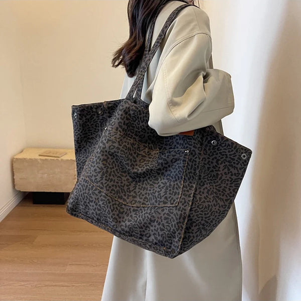 A woman holds a dark leopard print canvas tote bag against a light-colored shirt.