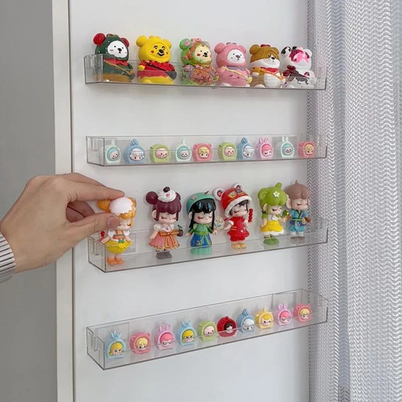 A hand places small, colorful figurines into a clear acrylic wall-mounted display shelf with multiple tiers.