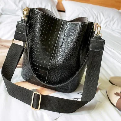Black vintage alligator pattern crossbody bag resting on white bedding.
