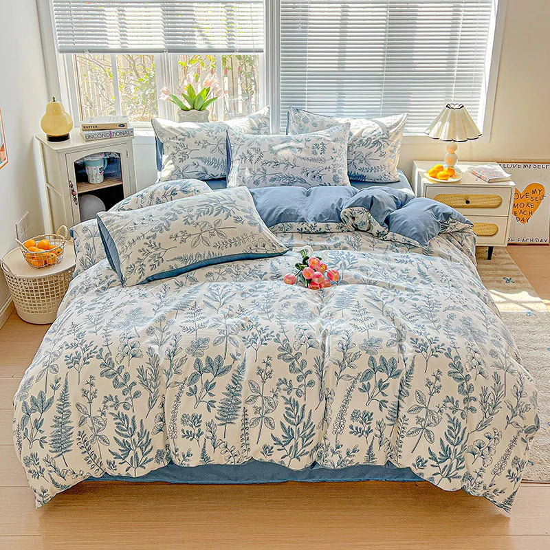 A light blue floral duvet cover set with a patterned quilt and pillows displayed on a bed.