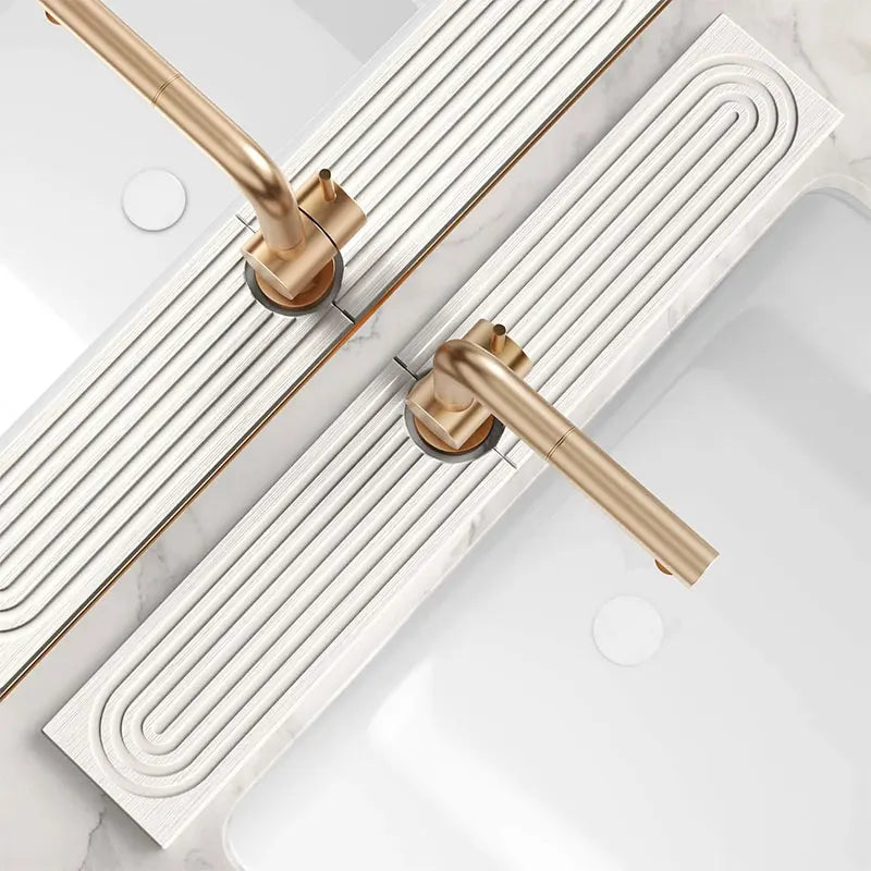 A close-up view of a gold-toned quick-dry diatomite faucet mat installed on a white marble countertop.