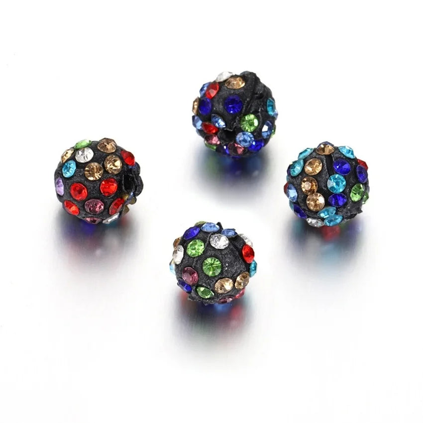 Four dark, round beads encrusted with various colored crystals are displayed on a white surface.
