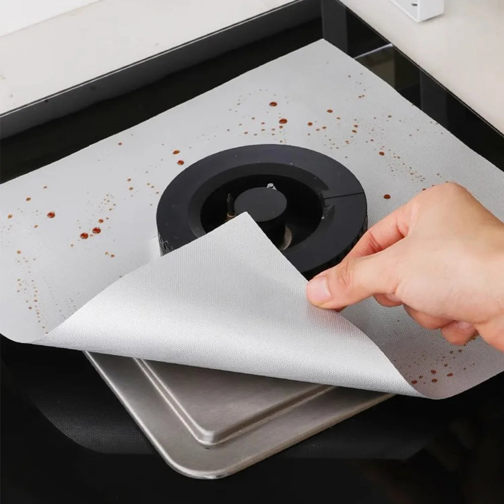 A hand places a white cloth over a black stove burner cover with scattered reddish-brown residue on the surface.
