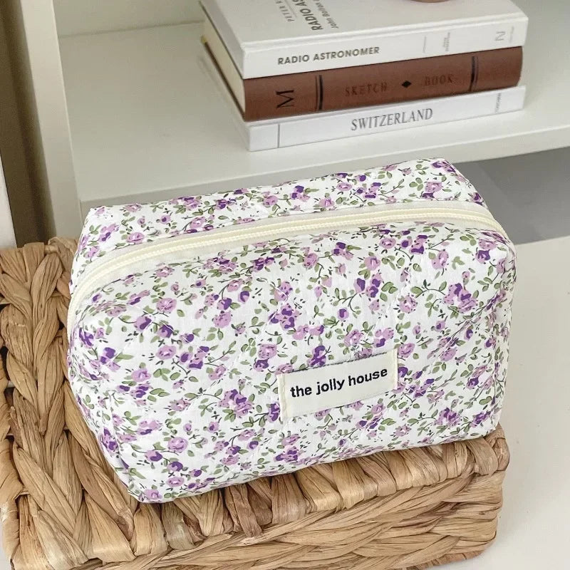 A floral quilted makeup bag with a purple and green pattern resting on a woven tray.