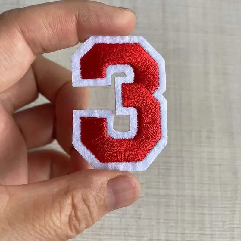 A hand holds a red and white iron-on 3D number patch for clothing.