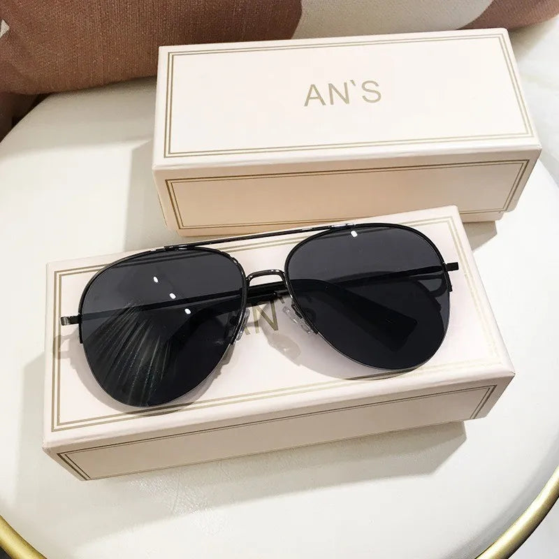 Eine schwarze Aviator-Sonnenbrille liegt auf einer hellbeigen Box mit der Marke AN'S.
