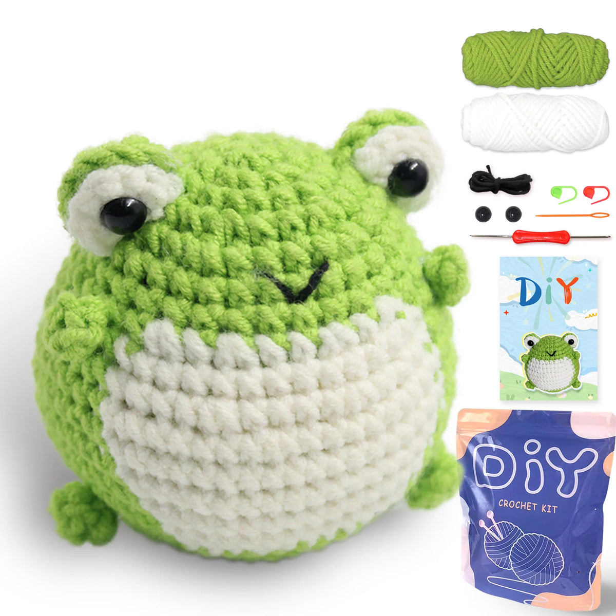 A crocheted green and white frog amigurumi toy with black eyes and a small stitched mouth, shown next to yarn and tools.