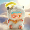 A fluffy white monster plush toy with yellow hair and blue accents sitting in a sandy outdoor setting.