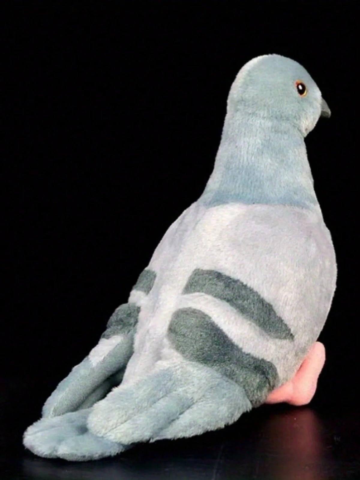 A soft gray plush toy of a pigeon with a light blue head and gray body, shown in profile against a black background.