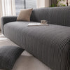 A dark gray quilted stretch sofa cover with a textured weave and a beige throw pillow on a light rug.