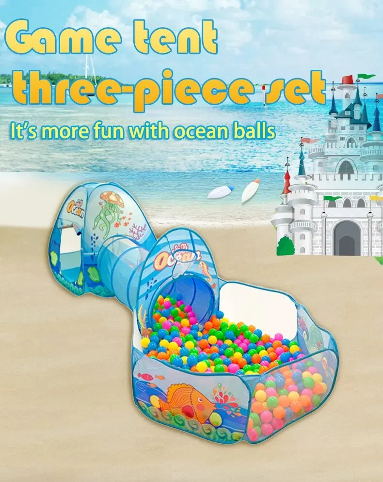 A colorful three-piece play tent with a tunnel and ball pit is set up on a sandy beach with the ocean in the background.