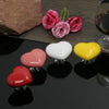 A collection of heart-shaped toilet flush buttons in shades of pink, red, and yellow, with some rose petals nearby.