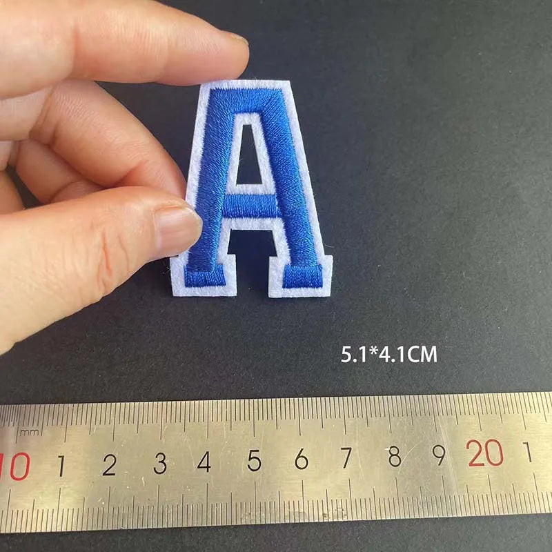 A letter patch embroidered in blue and white thread, measured at 5.1 x 4.1 cm.