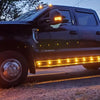 A black pickup truck with bright yellow LED side marker lights illuminated at dusk.