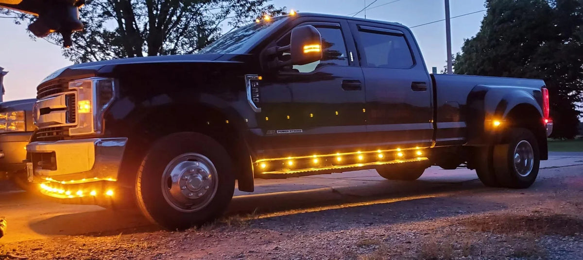 A black pickup truck with bright yellow LED side marker lights illuminated at dusk.