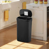 A black automatic touchless trash can with a lid open, sitting on a kitchen counter.